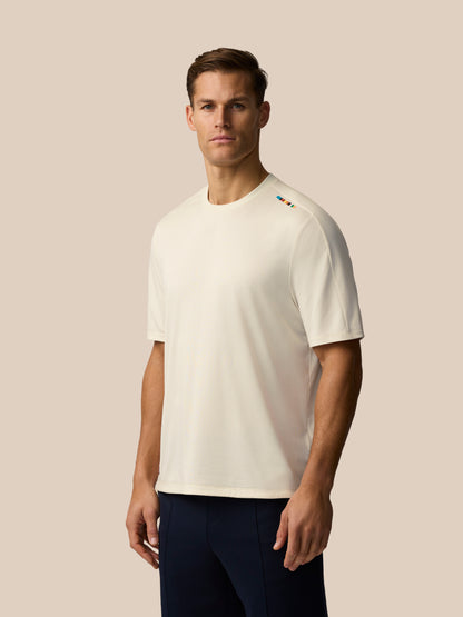 Three quarter view of a man wearing a cream knit T shirt with a colorful stripe on the left shoulder