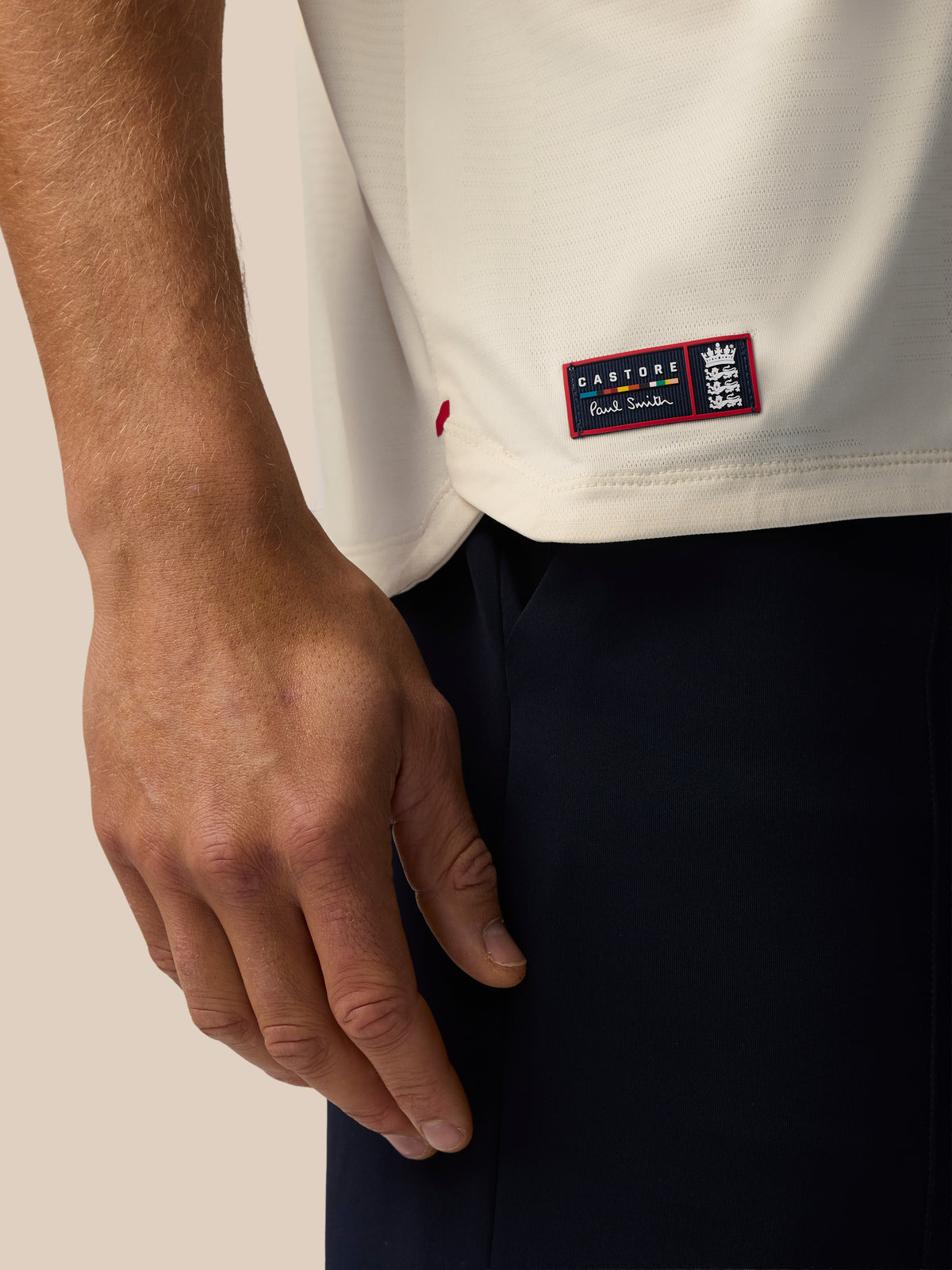 Close up of cream knit T shirt showing a red bordered Castore Paul Smith patch at the hem with an England crest.