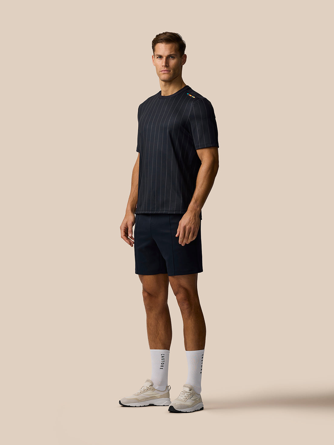 Full body side view of a male model in a dark pinstripe T-shirt with navy shorts and white socks