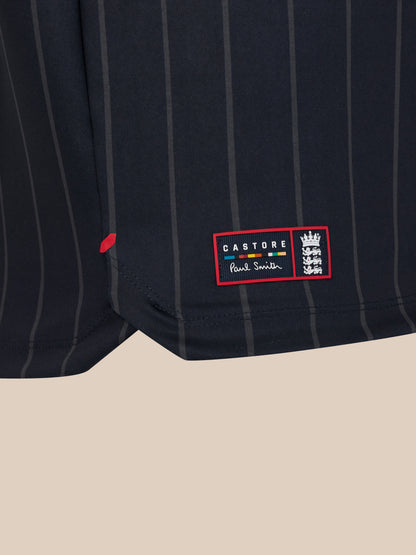 Close-up of navy pinstriped fabric from a Paul Smith x Castore England Cricket T-shirt with a red label patch featuring the Castore Paul Smith logo and ECB crest at the hem.