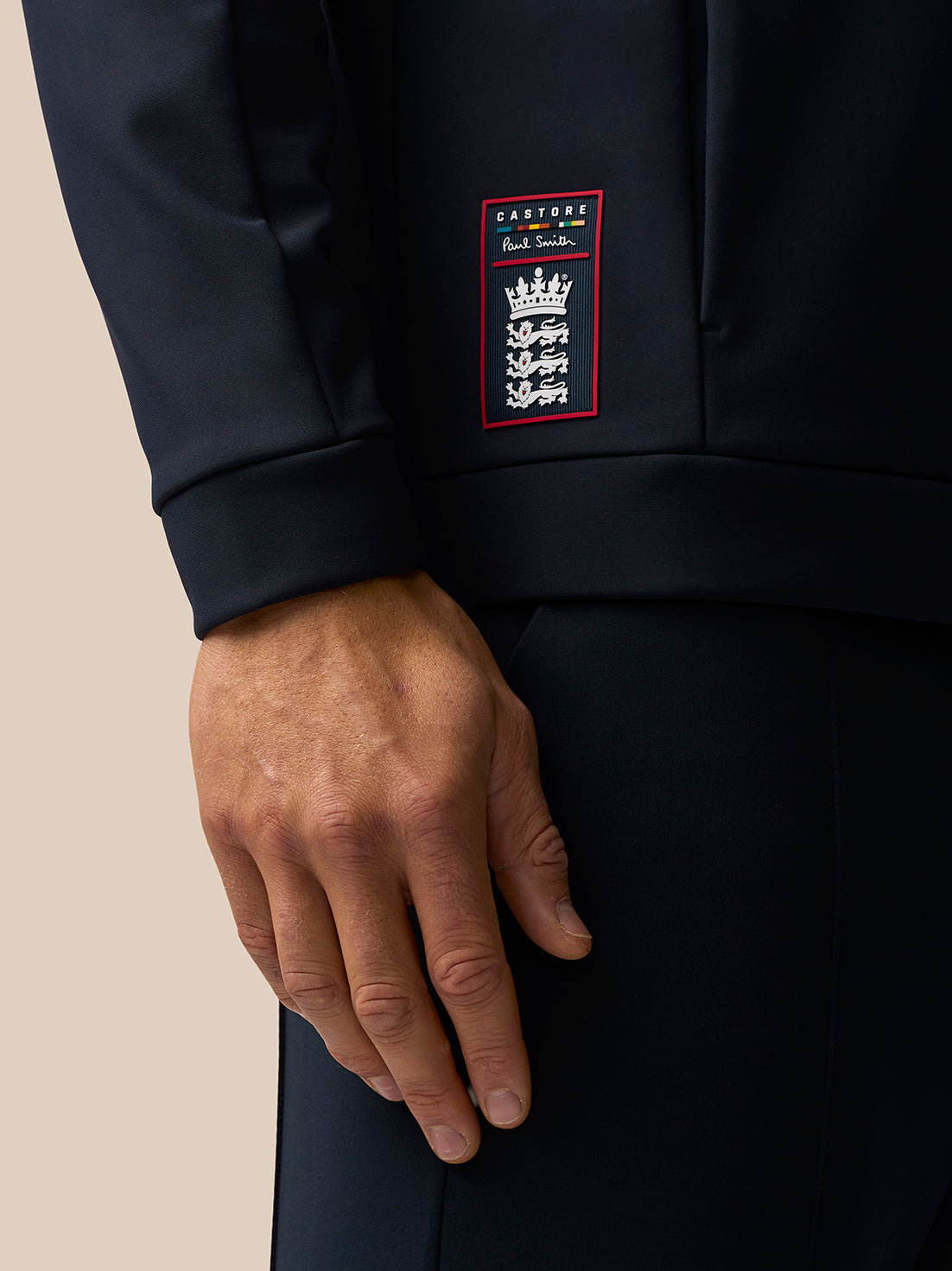 Close up of navy hoodie chest area showing the Castore Paul Smith badge and multicolor signature stripe