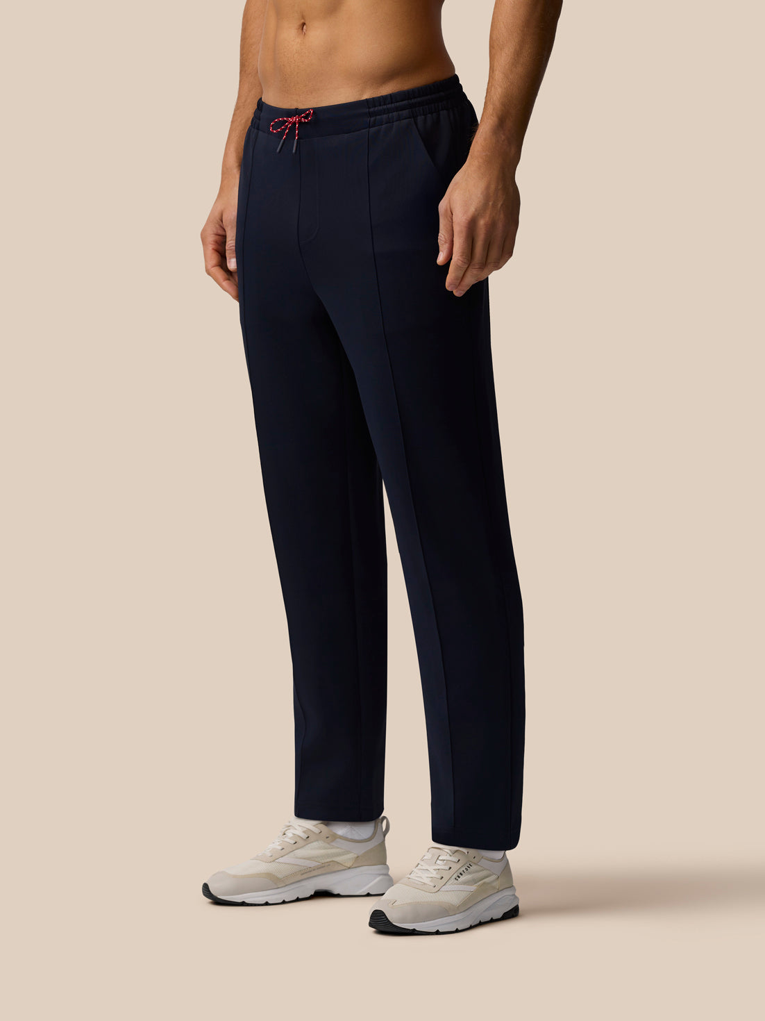 Model wears navy tailored unisex trousers with red drawcords and white sneakers