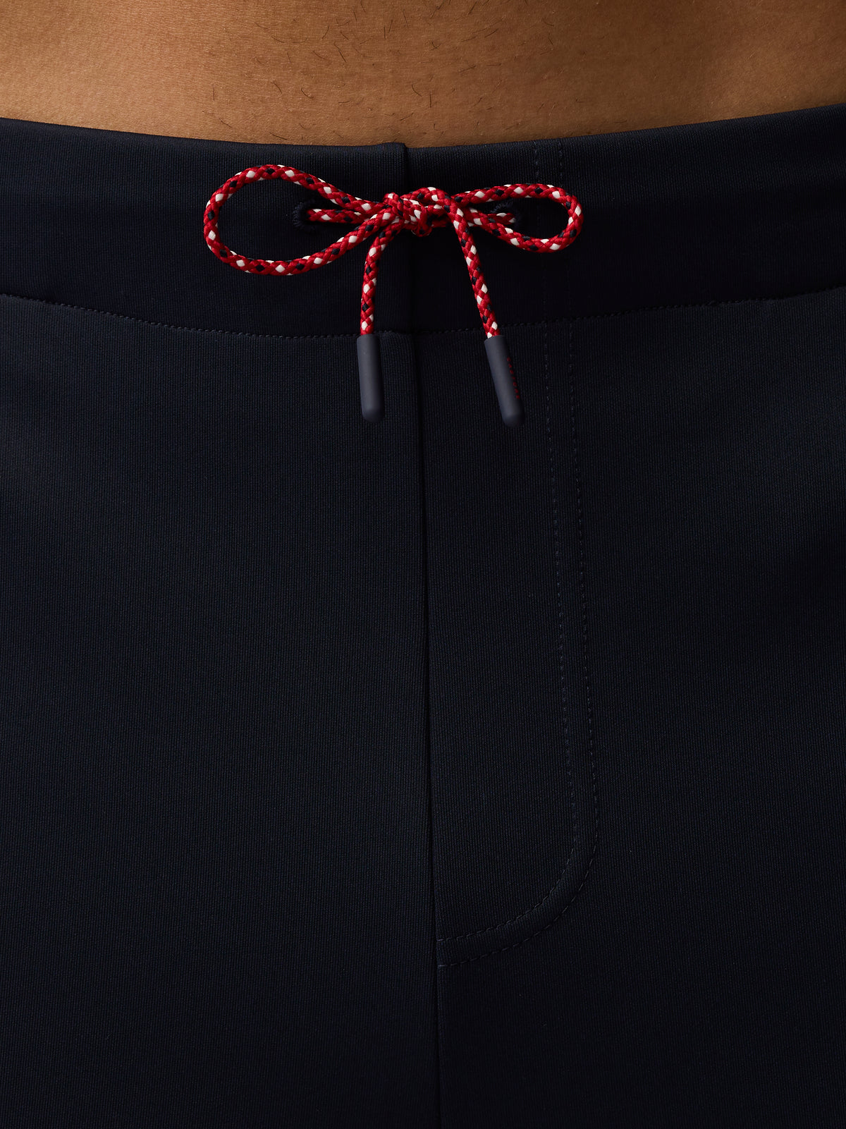 Close up of navy tailored trousers waistband with red white braided drawcords tied in a bow