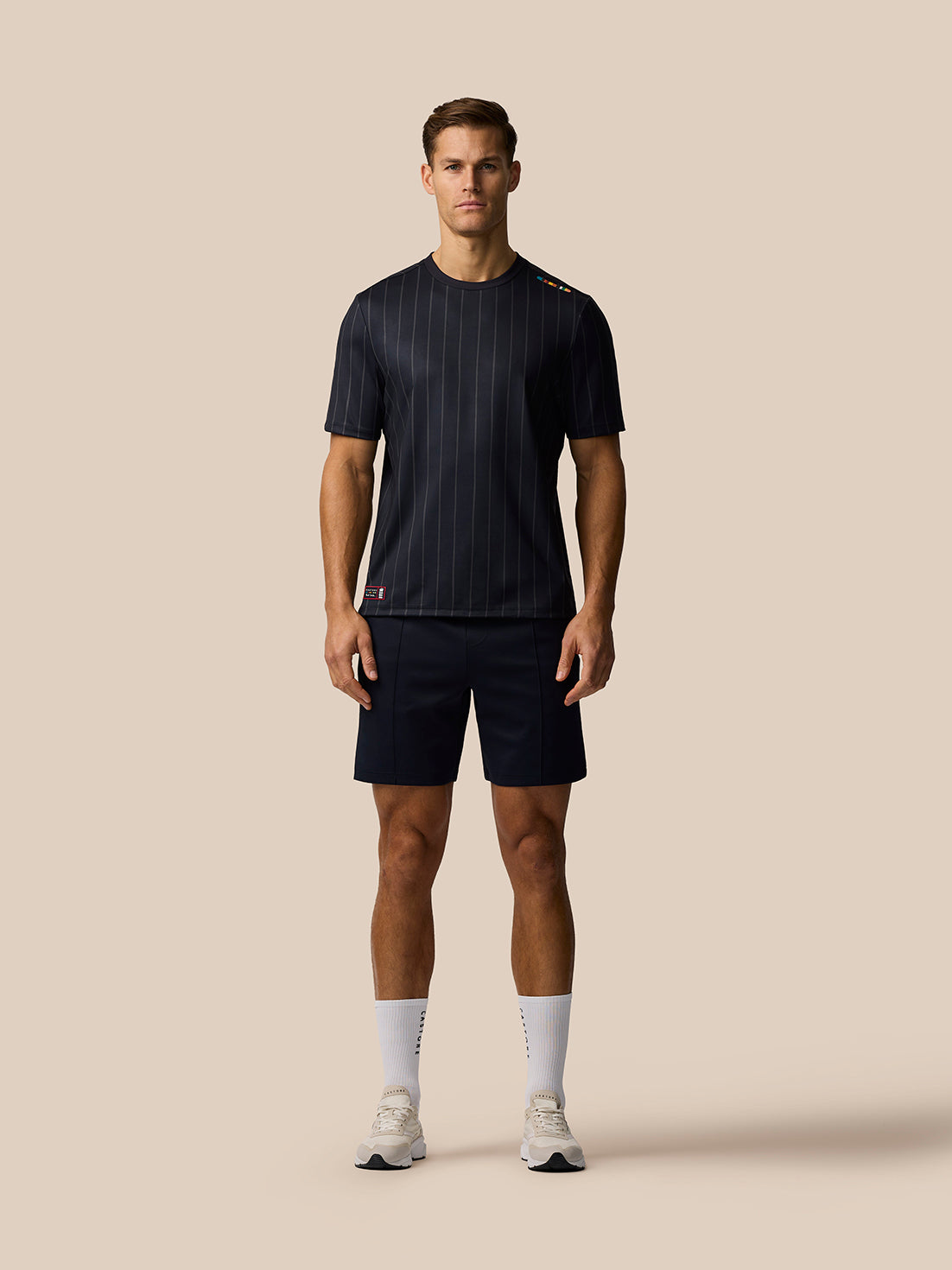 Male model wearing a dark navy pinstripe short sleeve top with matching navy shorts against a beige background.