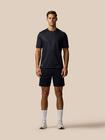 Male model wearing a dark navy pinstripe short sleeve top with matching navy shorts against a beige background.