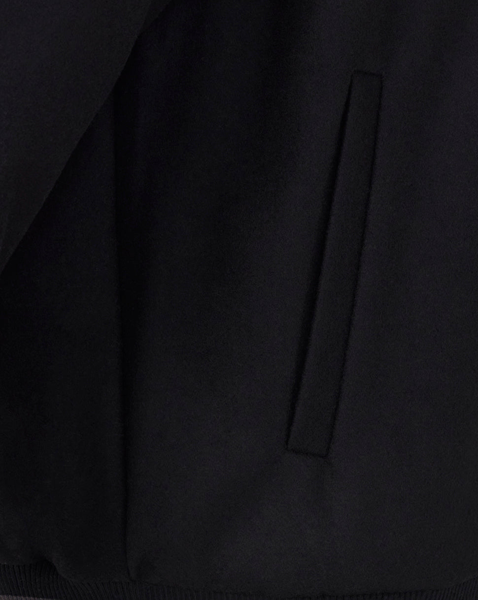 Close up of black bomber jacket fabric showing a vertical side pocket detail.