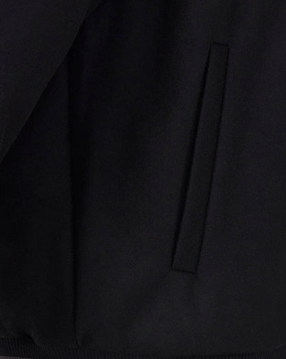 Close up of black bomber jacket fabric showing a vertical side pocket detail.