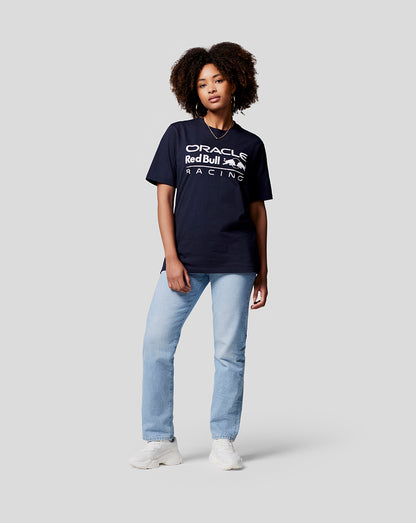 Full body shot of a woman in a navy Oracle Red Bull Racing T shirt paired with light jeans and white sneakers