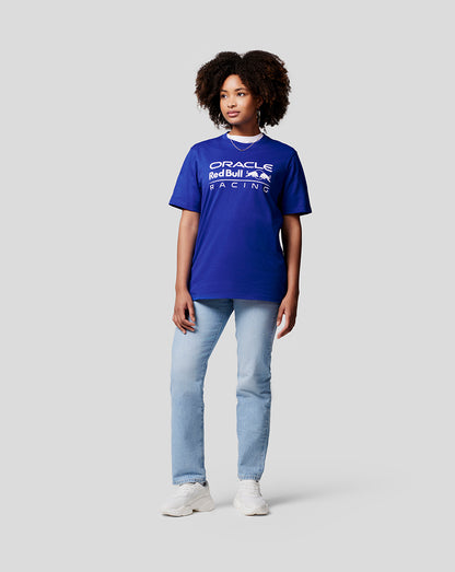 Woman wearing blue Oracle Red Bull Racing tee with white chest logo, denim jeans and white sneakers