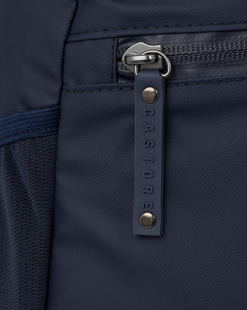 Close-up of navy backpack zipper with embossed Castore pull and metal hardware
