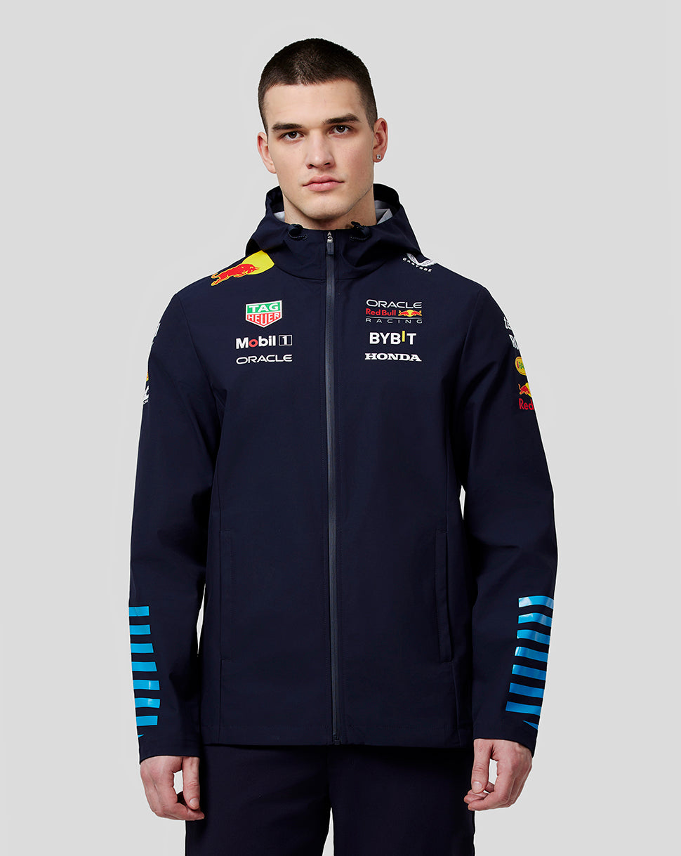 Man wearing navy water resistant jacket with sponsor logos and blue stripe details on sleeves