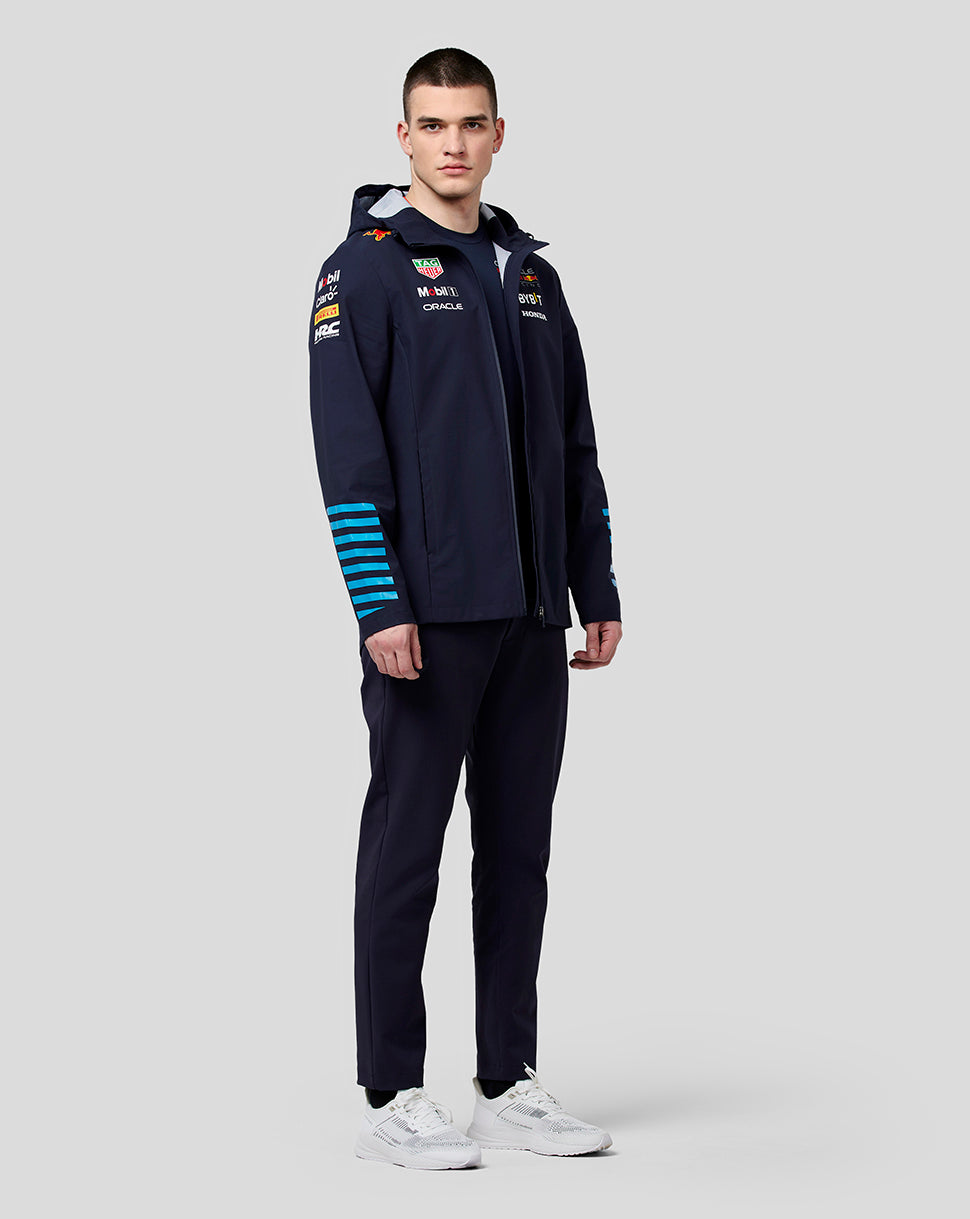 Full body shot of model in navy hooded water resistant jacket with blue stripes on the sleeves and white sneakers.