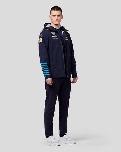 Full body shot of model in navy hooded water resistant jacket with blue stripes on the sleeves and white sneakers.