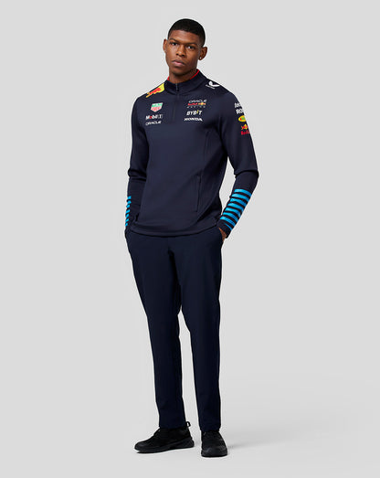 Front view of a male model wearing navy Red Bull Racing Teamline midlayer with quarter zip and sponsor logos on chest.