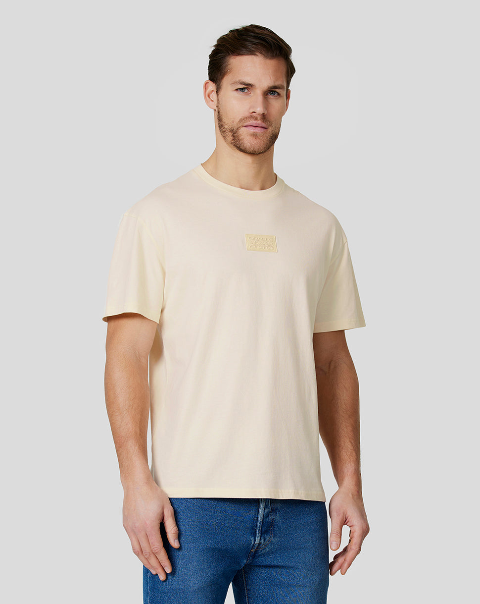 Male model wearing a cream unisex tonal oversized tee with a chest patch logo