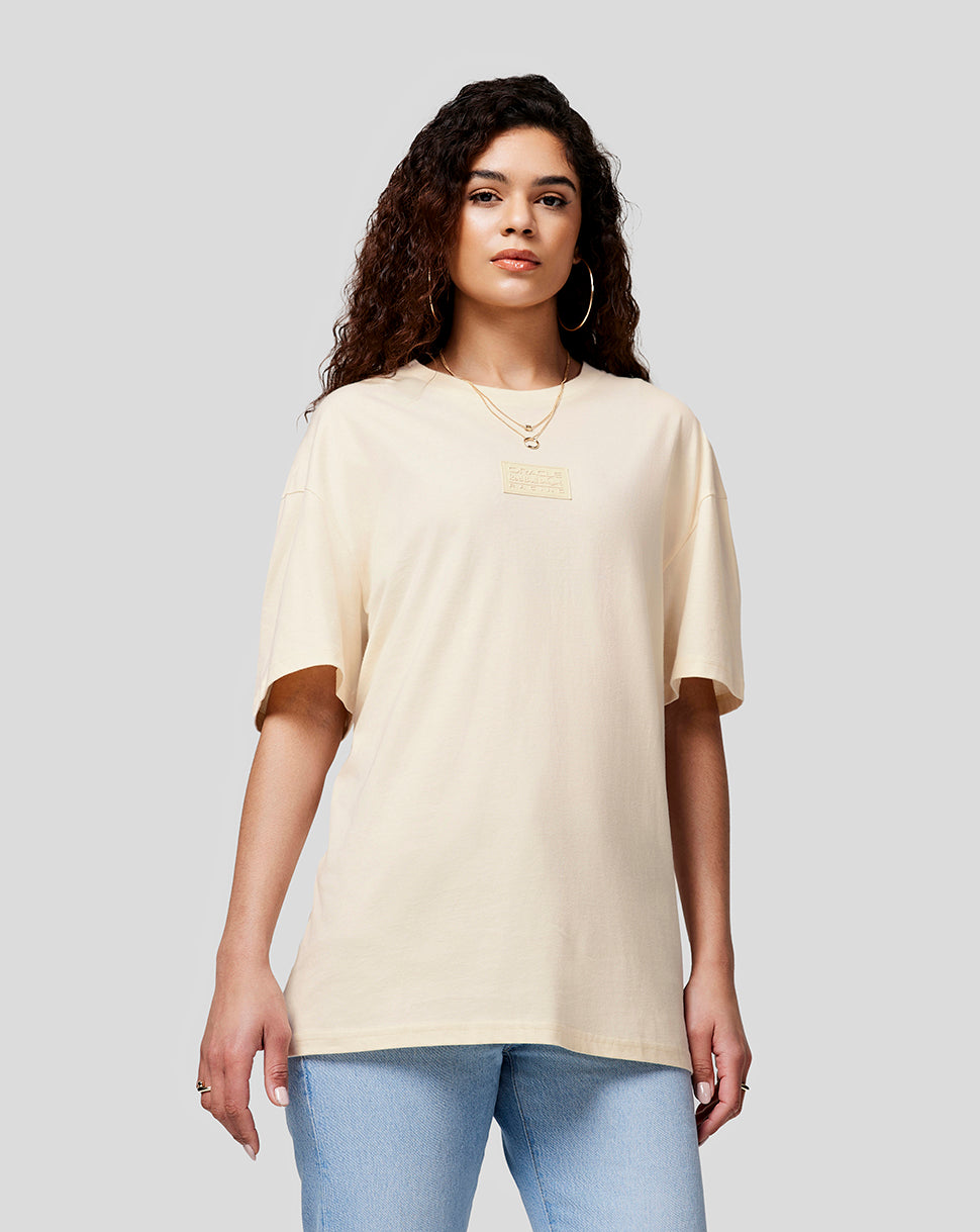 Female model wearing a cream tonal oversized tee with a chest patch logo