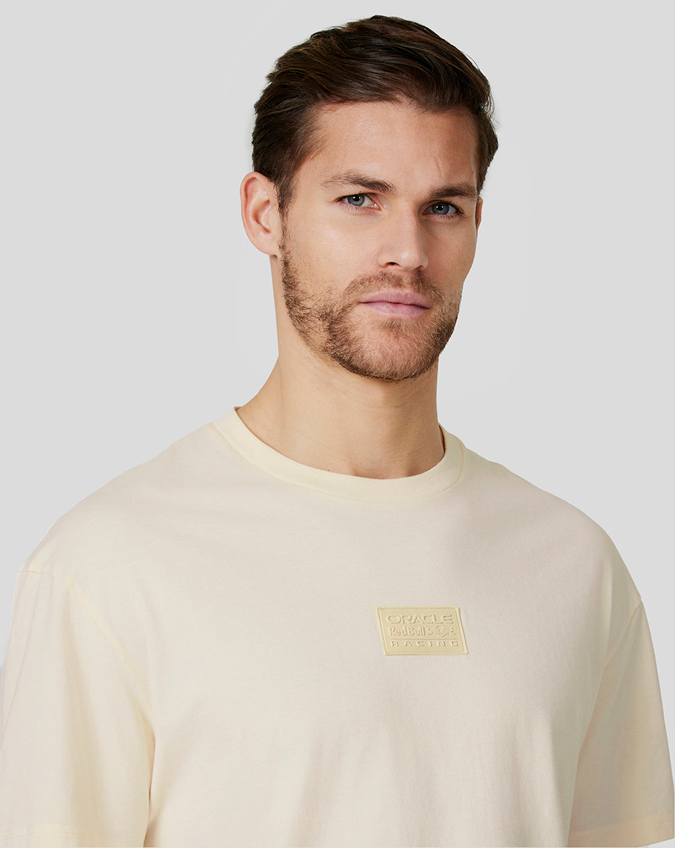 Cream oversized crewneck T shirt with a small chest patch logo worn by a man
