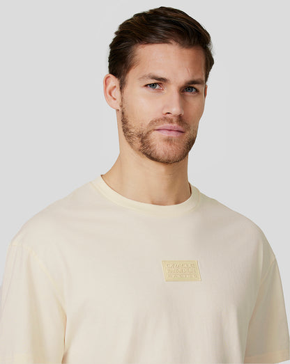 Cream oversized crewneck T shirt with a small chest patch logo worn by a man