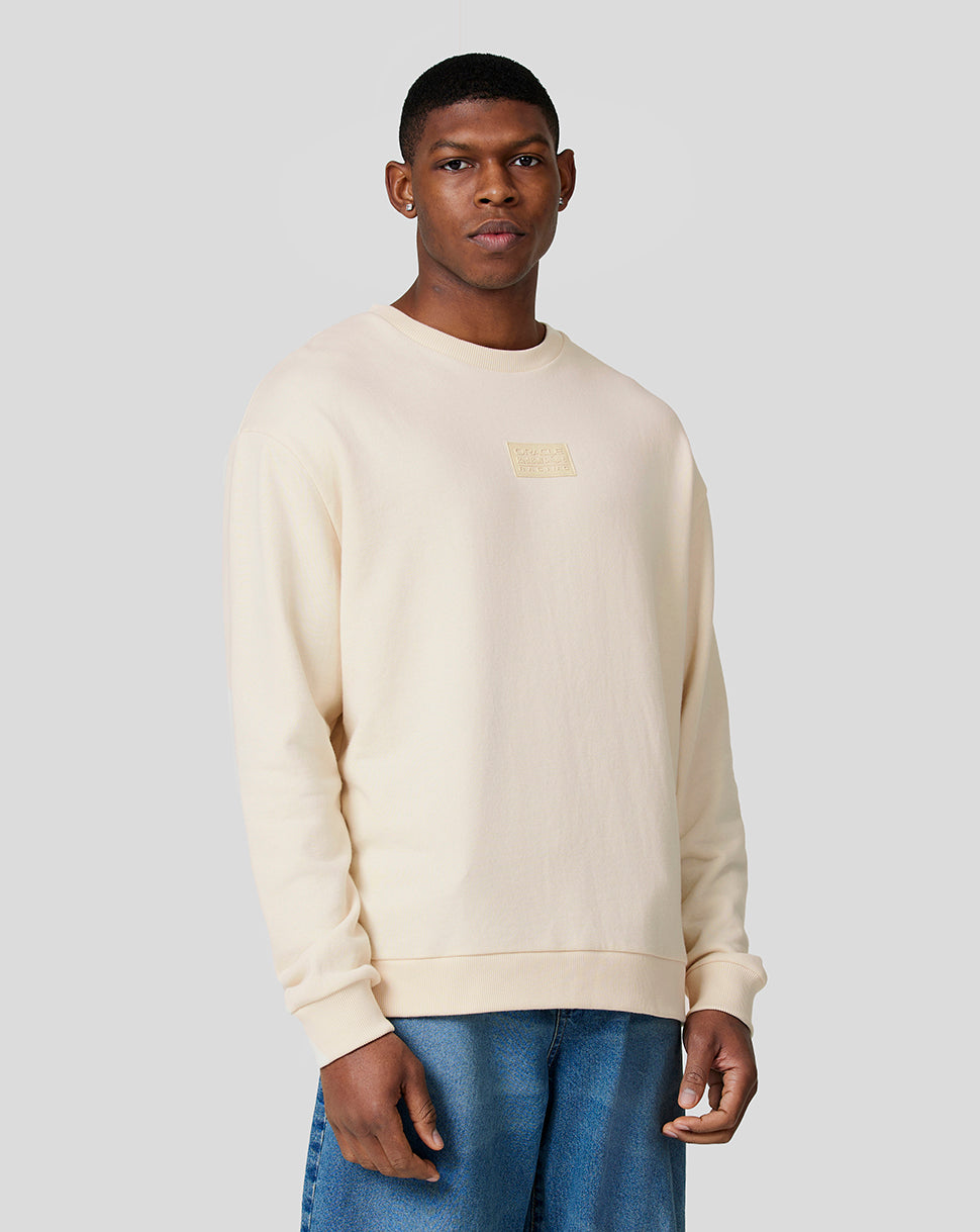 Full-body shot of a male model in an ecru oversized crew neck sweatshirt with a chest patch, paired with blue jeans