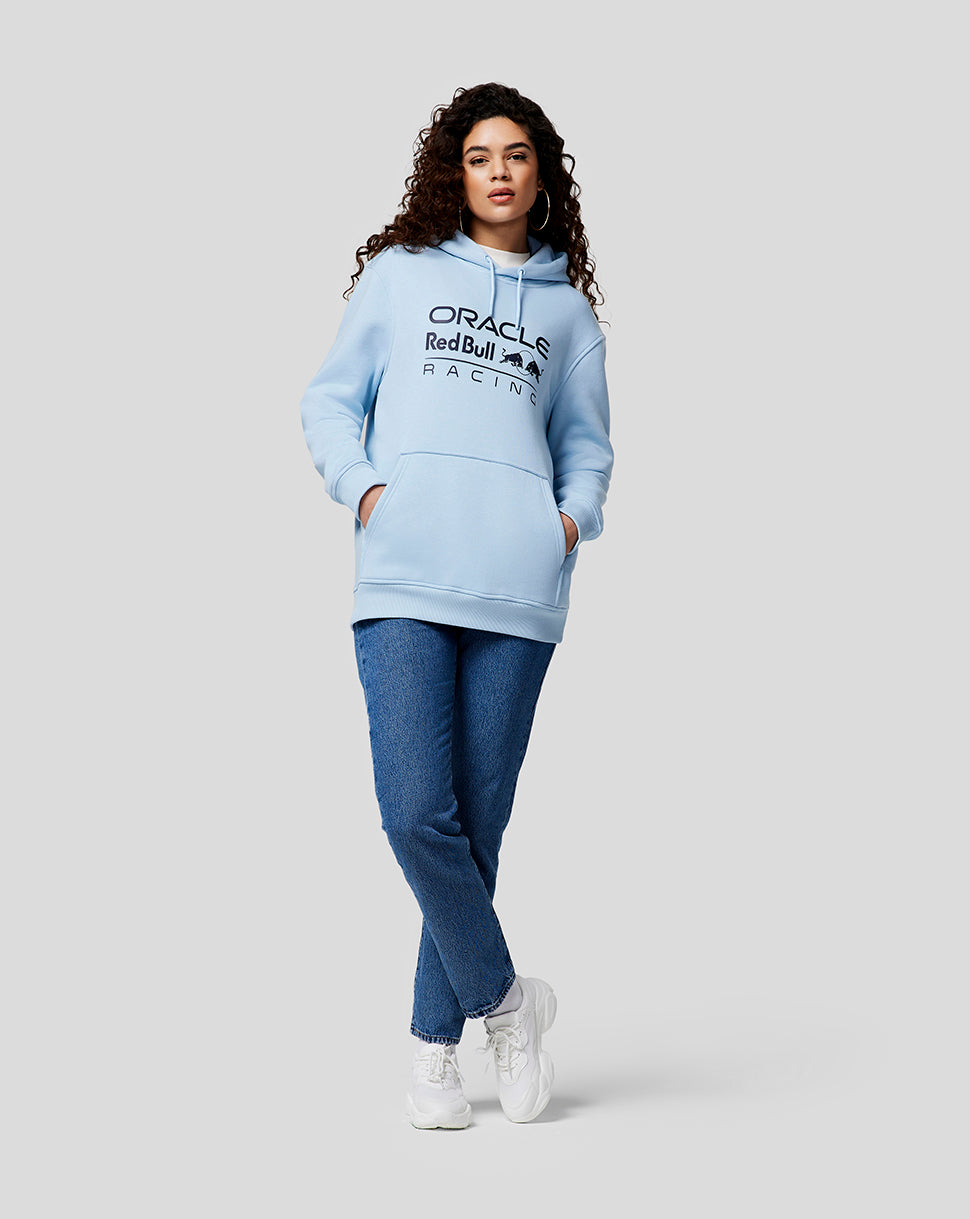 Woman in Dream Blue Oracle Red Bull Racing hoodie with chest logo posing with hands in pockets.