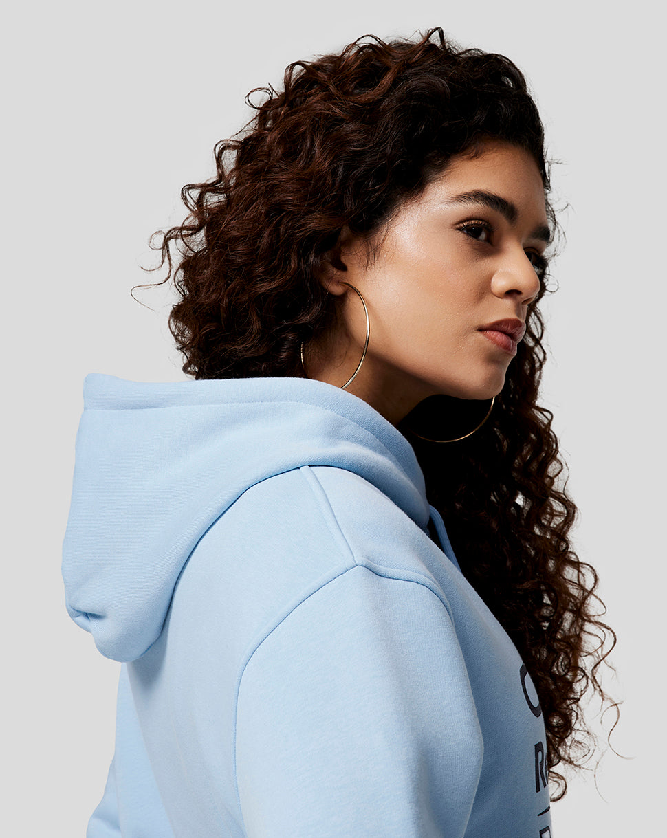 Side profile of a woman wearing a light blue Oracle Red Bull Racing hoodie with hood up and logo on chest