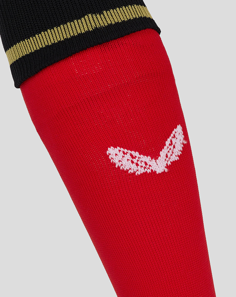 Close up of red Mk Dons junior away sock showing white wing logo and black cuff with gold stripe.
