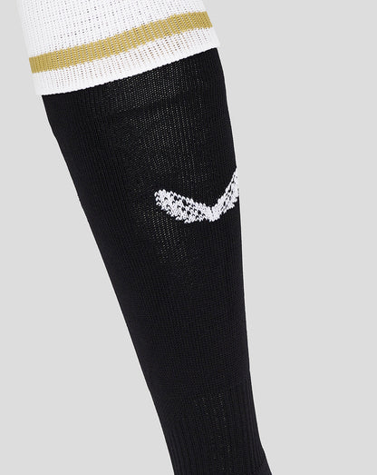 Close-up of Mk Dons third sock on leg with black fabric white logo and white cuff with gold stripe