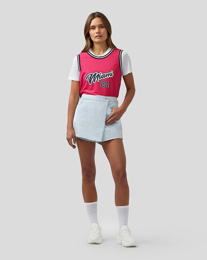 Full body shot of a model wearing a bright pink Miami basketball jersey with white tee underneath and denim skirt