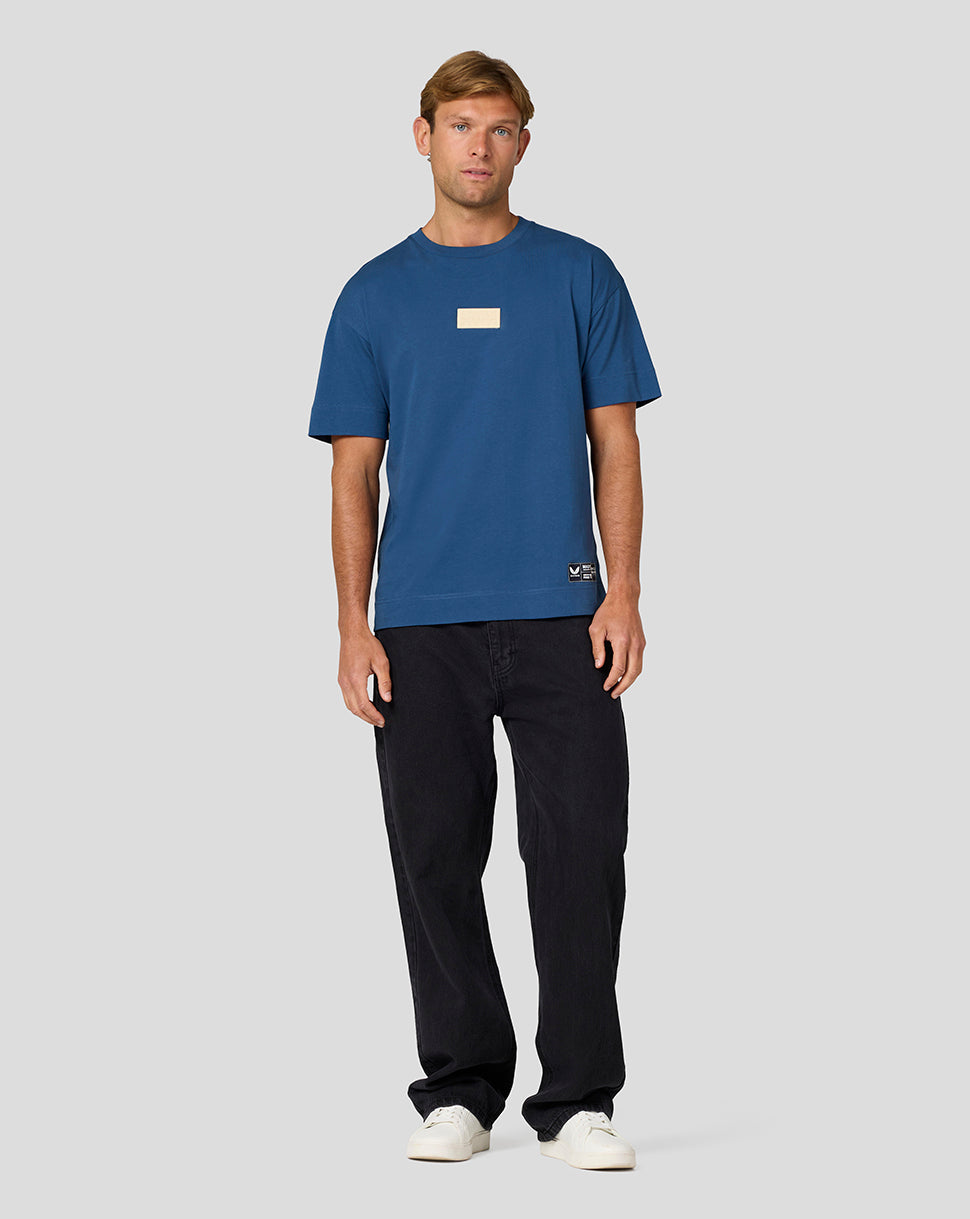 Full-body shot of a man in a blue Oracle Red Bull Racing Austin T shirt with a small beige chest patch