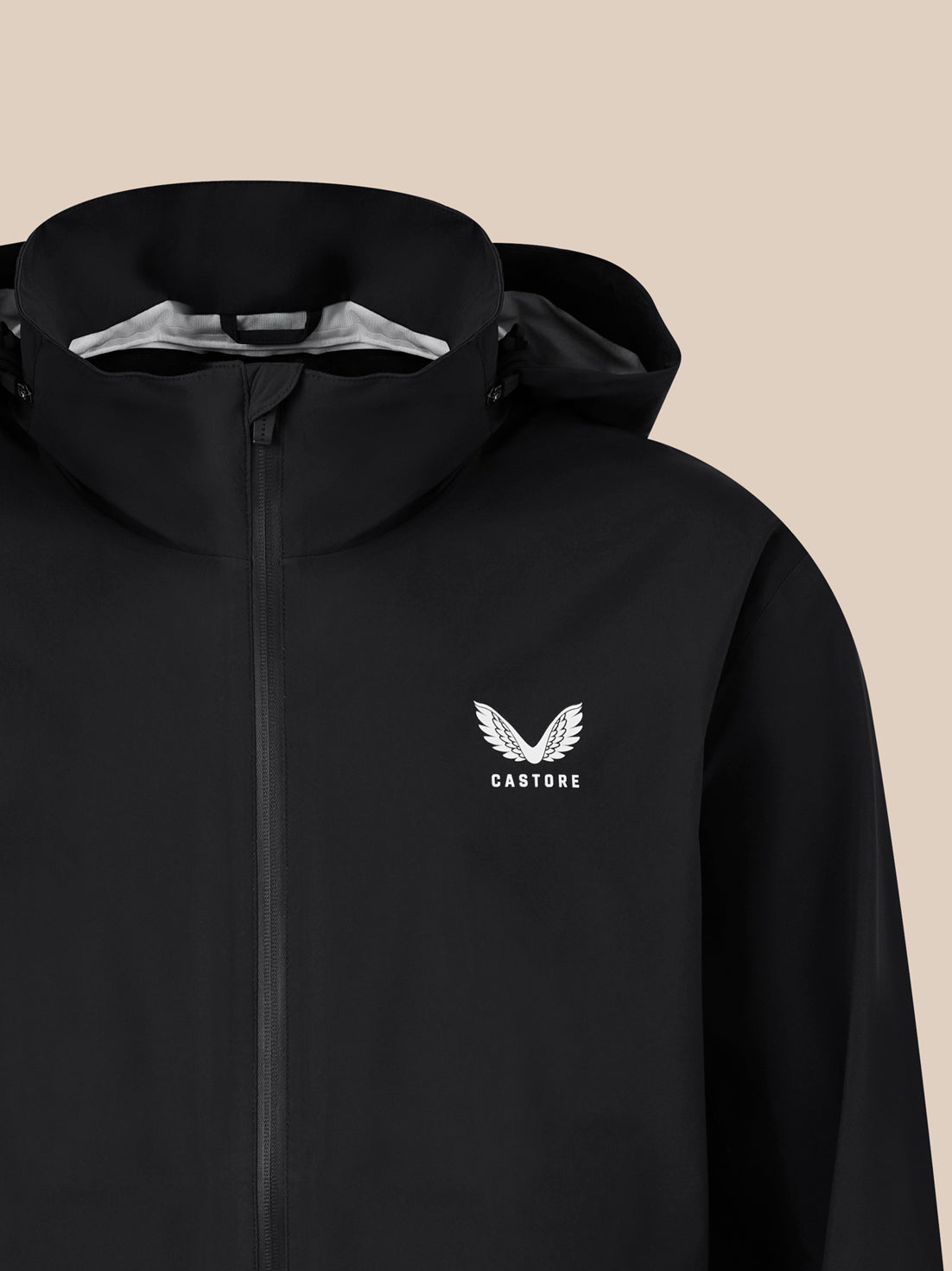 Close-up of a black waterproof jacket with a high collar and front zipper, Castore logo with wings on the chest.