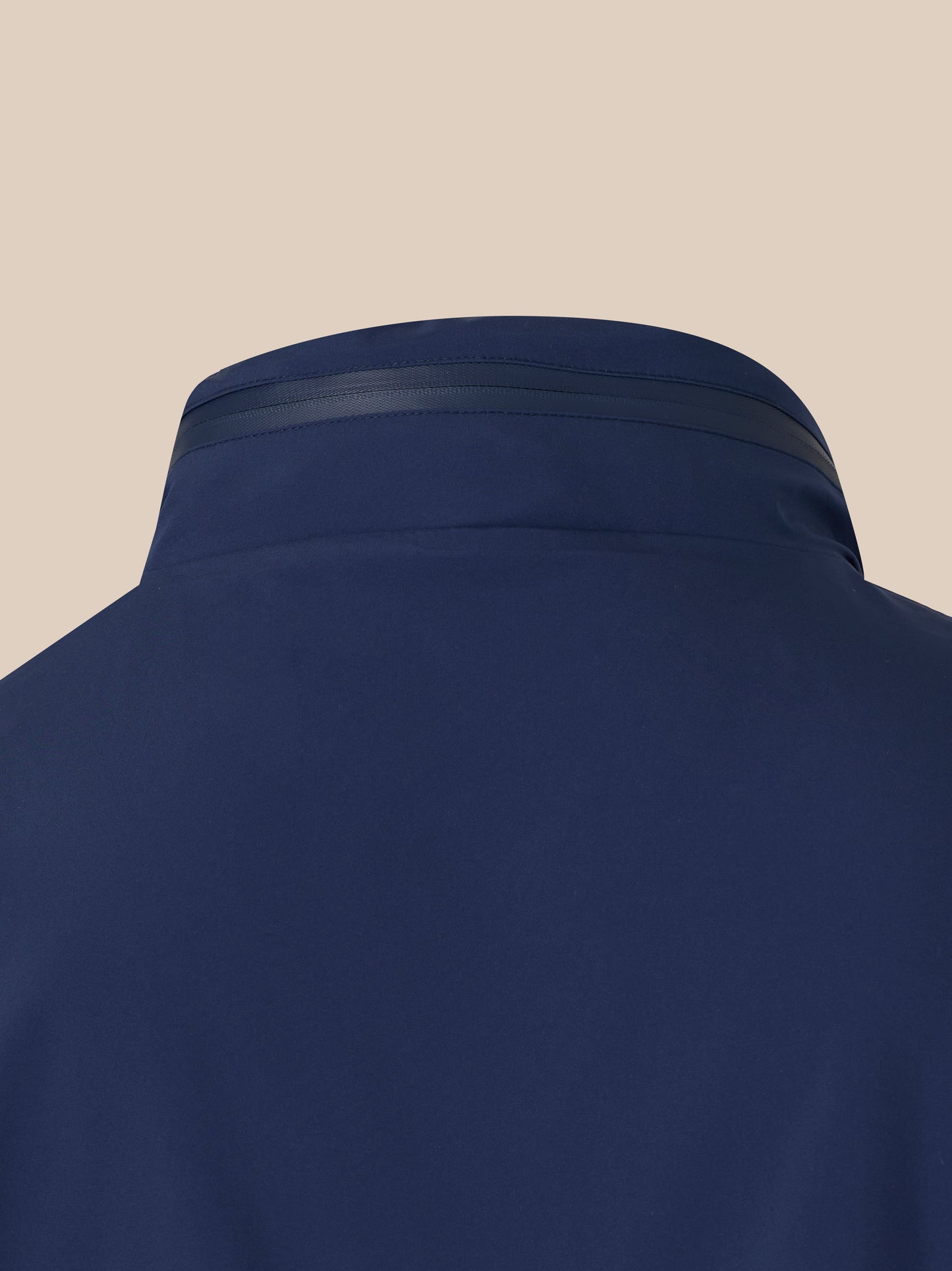 Close up of navy waterproof jacket hood with seam detailing against a beige background