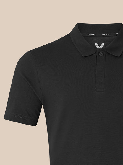 Close-up of black unisex polo showing ribbed collar and chest embroidery with the Castore logo