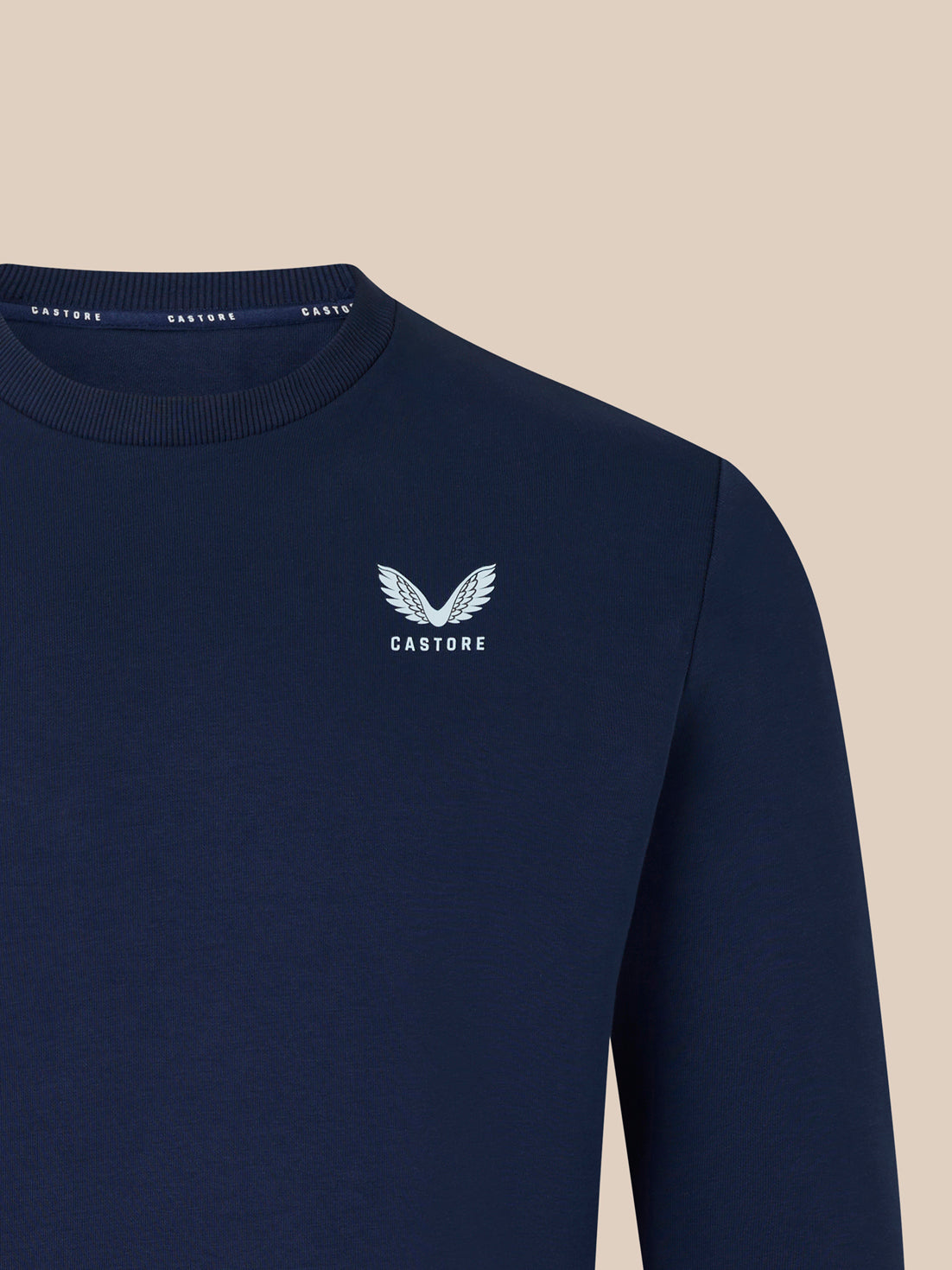 Navy crewneck sweatshirt close up shows the white wing logo and Castore branding on the chest.