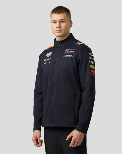 Three-quarter view of male model in navy Teamline Soft Shell Jacket showing front chest logos and zip pockets.