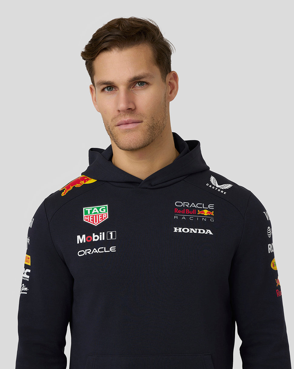 Side profile of a man in a navy Red Bull Racing hoodie with sleeve sponsor logos and a large Red Bull emblem on the back.