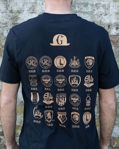 Back of navy Gentry Day T shirt with a large top hat shaped G logo and rows of circular club crests with dates across the back
