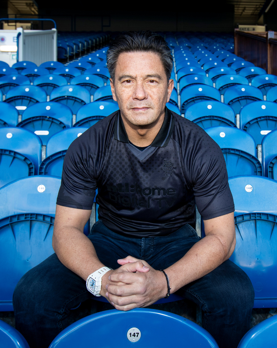 Man wearing black Rangers Retro 2002-03 Home Blackout shirt seated in blue stadium seats