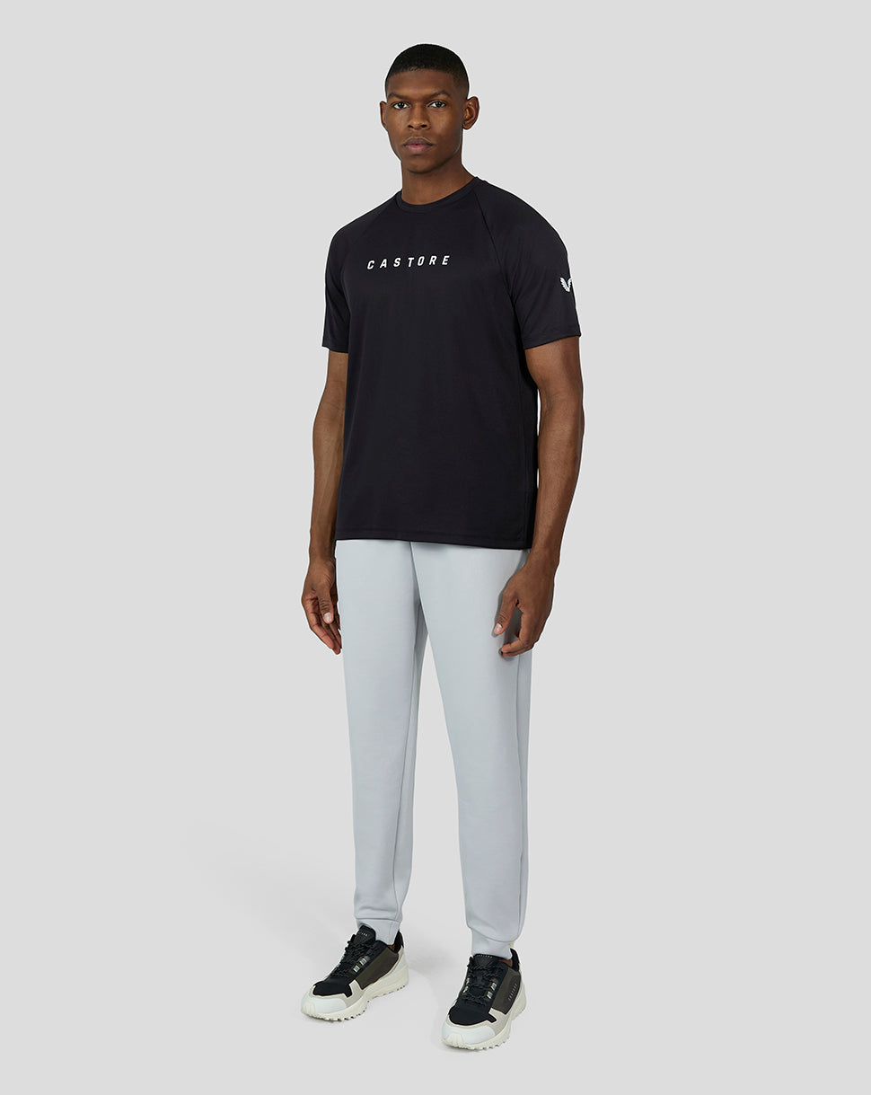 Male model wearing black short sleeve raglan tee with Castore branding on chest and sleeve, paired with light gray joggers.