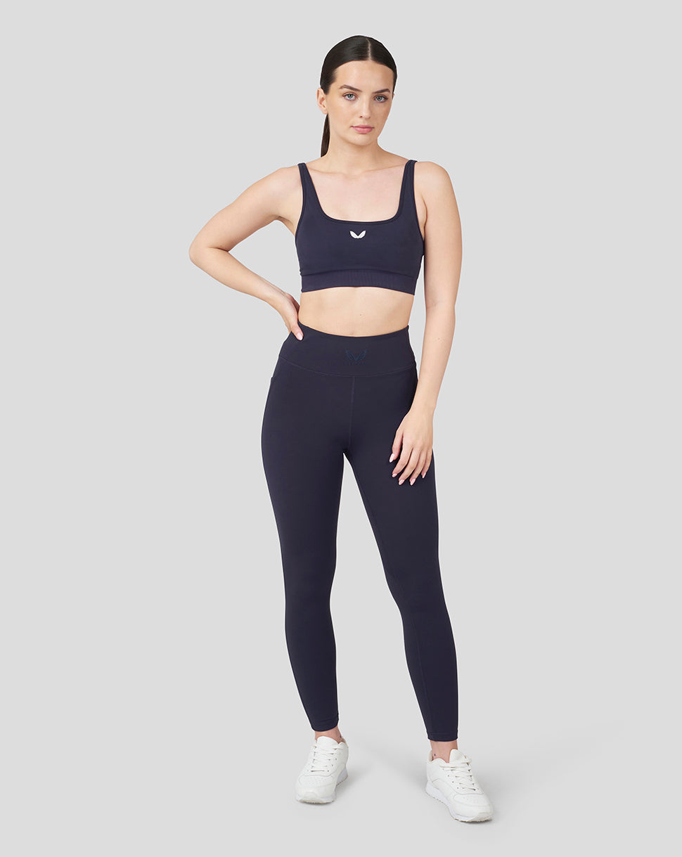 Model wearing navy Oracle Red Bull Racing running leggings and matching sports bra, standing with one hand on hip
