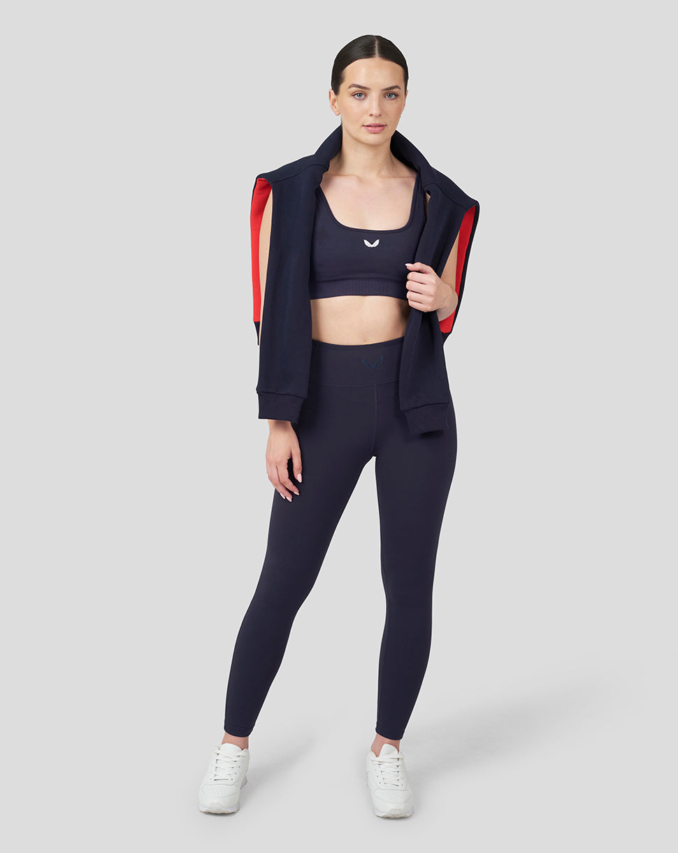 Full body front shot of a model in Oracle Red Bull Racing Night Sky leggings with a navy jacket featuring red sleeve accents.