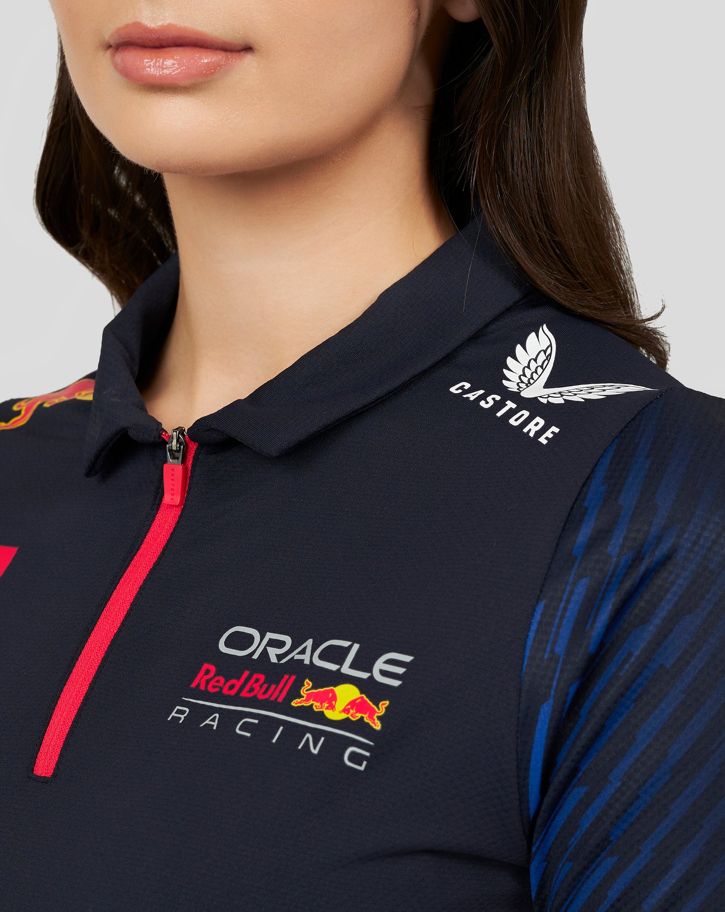 Close-up of a navy Oracle Red Bull Racing women's polo with a pink zipper, featuring Castore logo and Oracle Red Bull Racing branding
