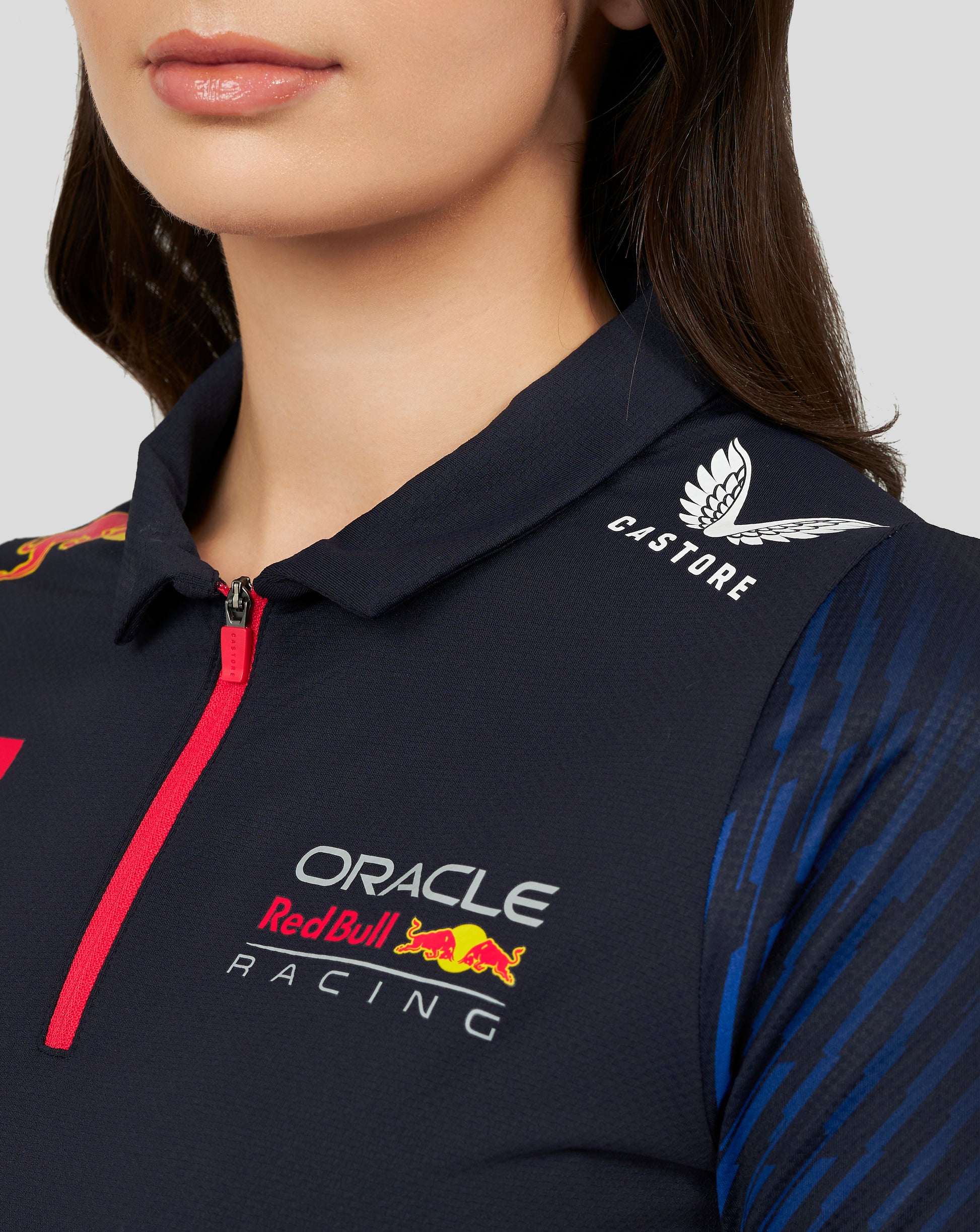 Close-up of a navy Oracle Red Bull Racing women's polo with a pink zipper, featuring Castore logo and Oracle Red Bull Racing branding