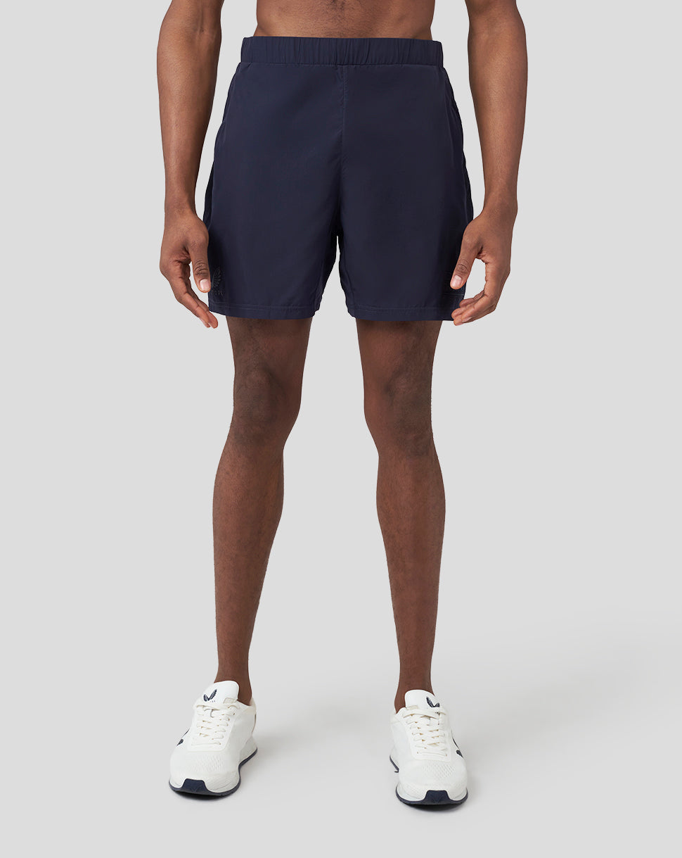 Front view of a male model wearing navy Oracle Red Bull Racing running shorts with white sneakers.