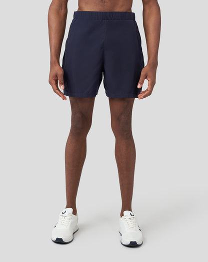 Front view of a male model wearing navy Oracle Red Bull Racing running shorts with white sneakers.