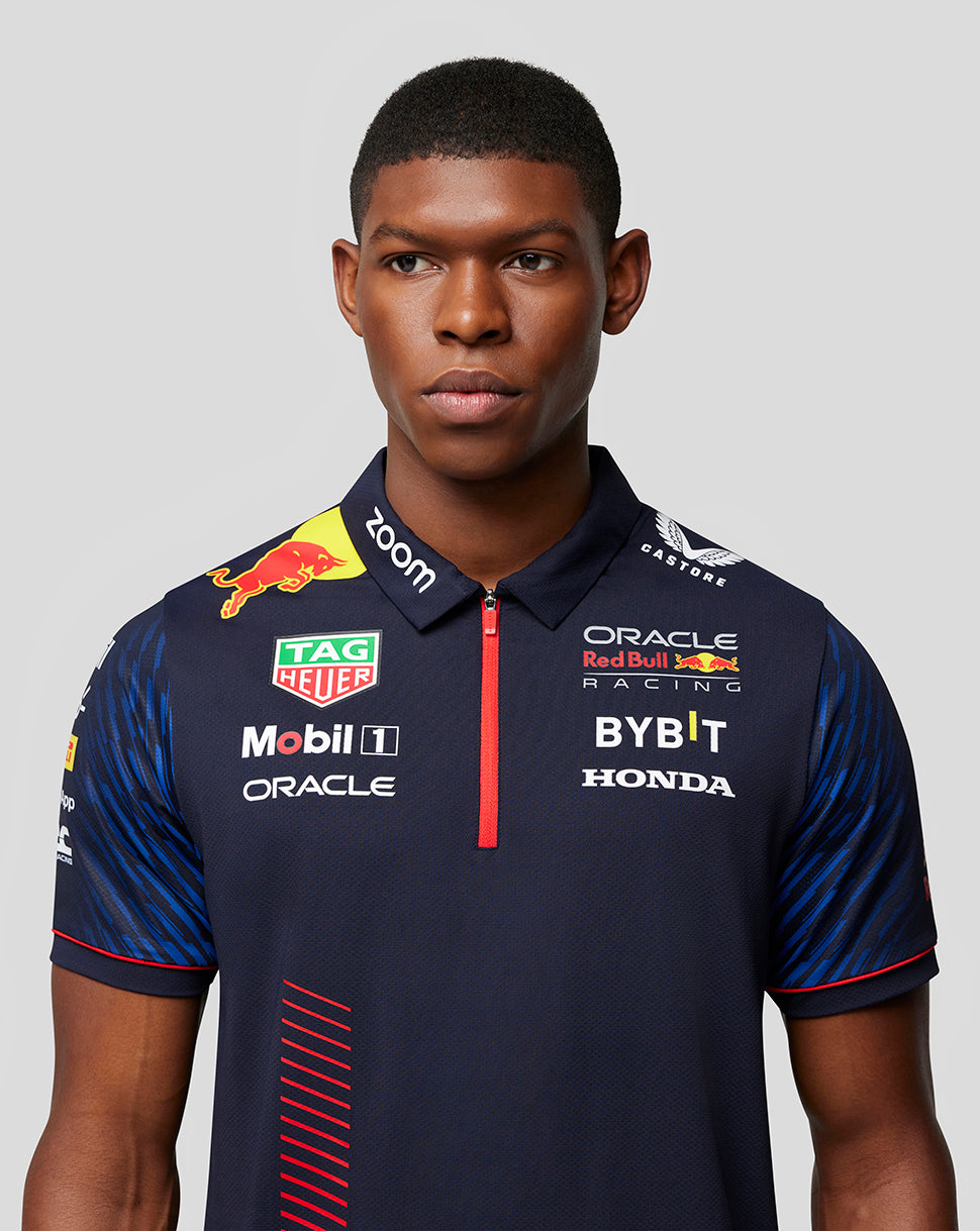 Male model wearing a Night Sky navy Castore x Oracle Red Bull Racing polo with sponsor logos and a red zip placket.