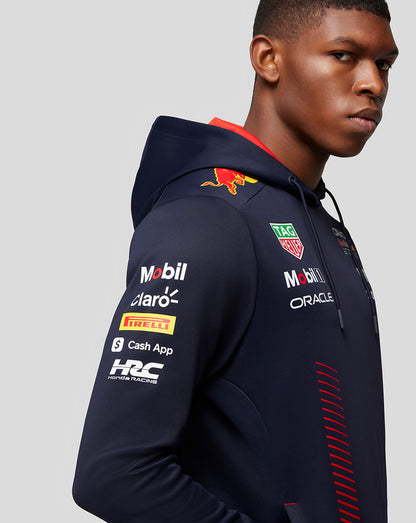 Side profile of a man in a navy Red Bull Racing hoodie with multiple sponsor logos on the chest and sleeve.