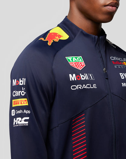 Close up of navy Red Bull Racing jacket on a model showing the shoulder logo and prominent sponsor patches