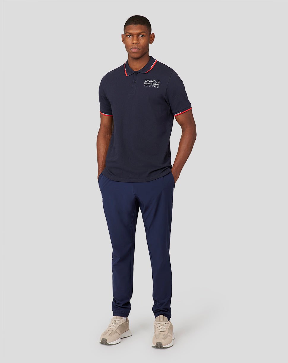 Full body shot of a man wearing navy Night Sky Oracle Red Bull Racing Core Polo with chest logo and red collar trim.