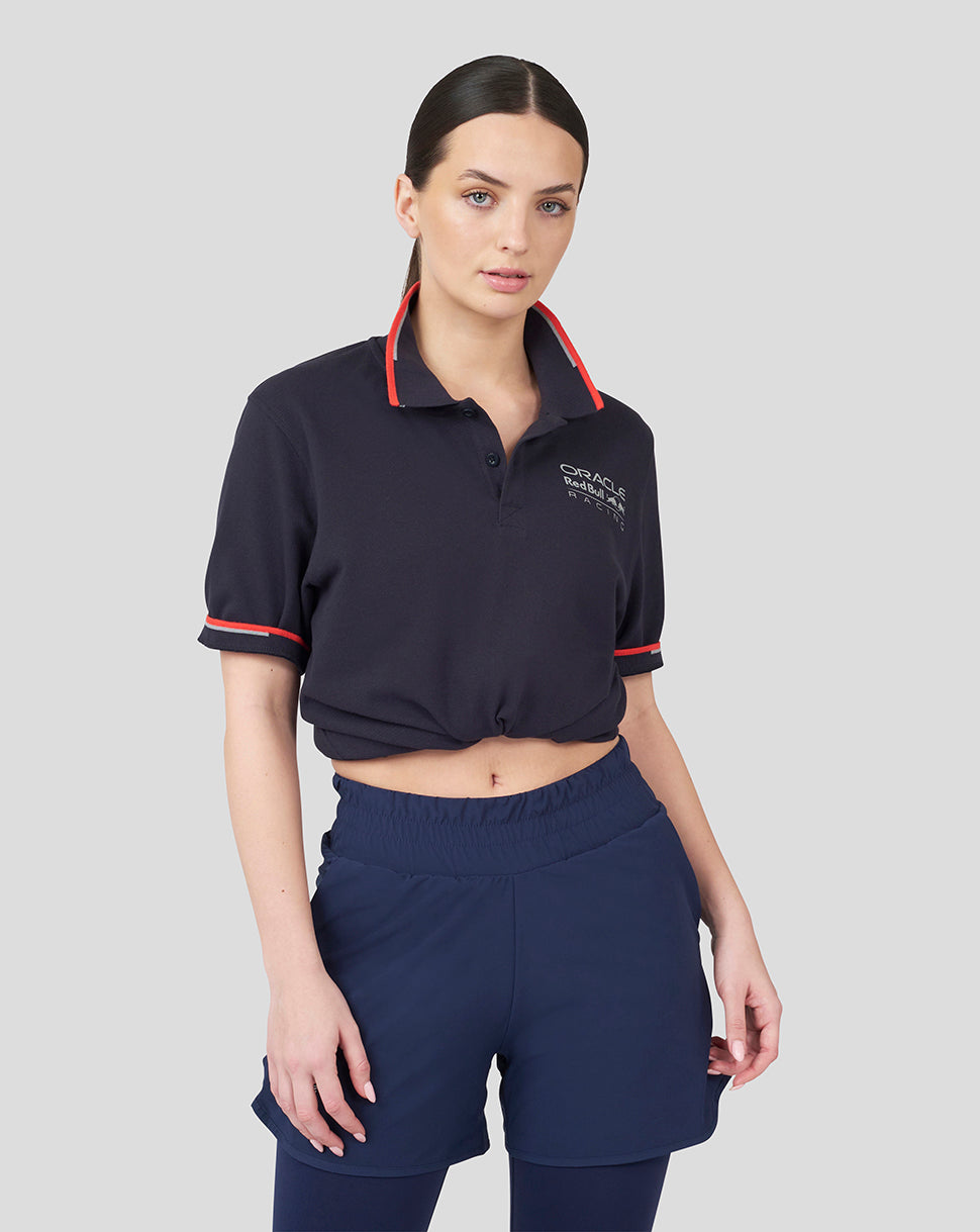 Female model wearing navy Oracle Red Bull Racing Core Polo with red collar trim and red sleeve piping, logo on chest