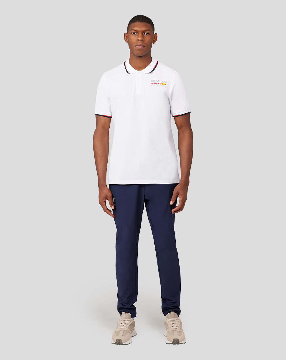 Male model in white Oracle Red Bull Racing Core Polo with left chest logo, paired with navy pants.